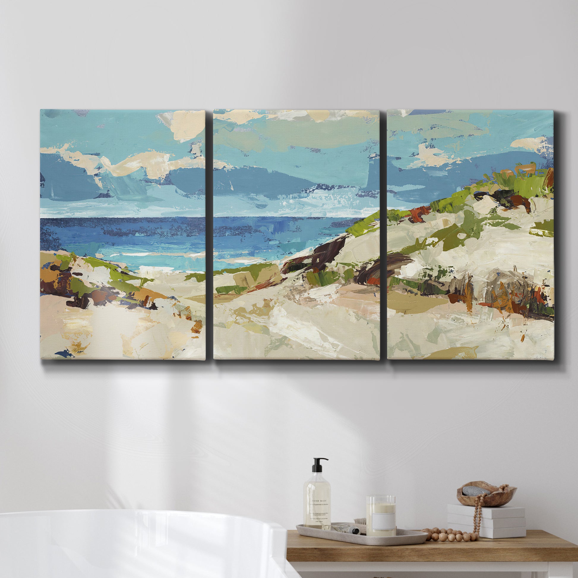 Three-panel canvas wall art featuring sand dunes beside open water, displayed in a bathroom above a bathtub.