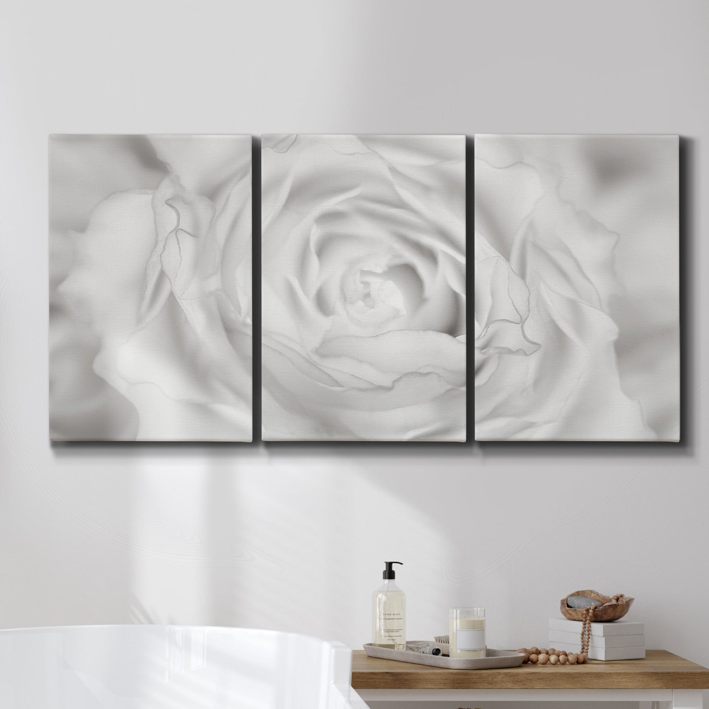 Three-panel canvas wall art featuring monochrome rose study photograph, displayed in a bathroom above a bathtub.