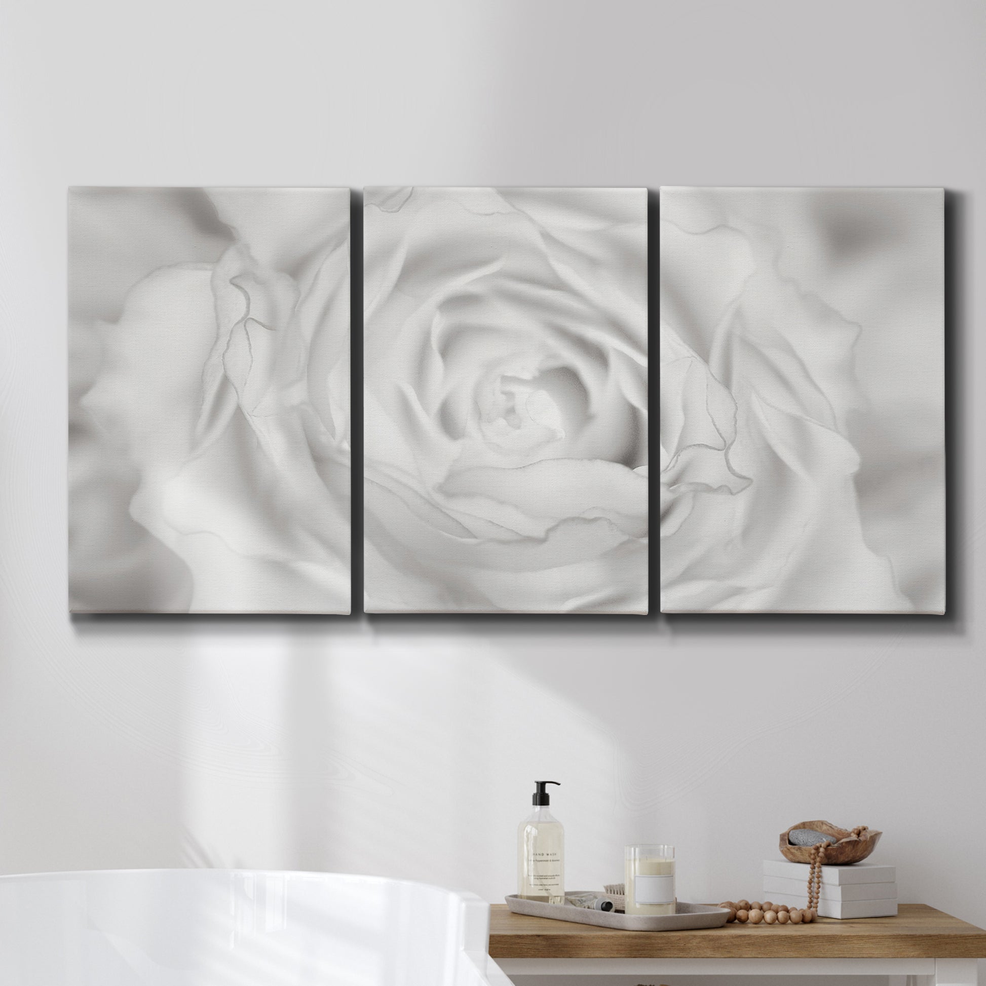 Three-panel canvas wall art featuring monochrome rose study photograph, displayed in a bathroom above a bathtub.