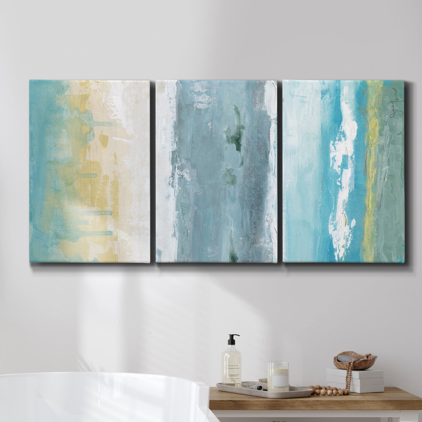 Three-panel canvas wall art featuring abstract coastal shoreline textures, displayed in a bathroom above a bathtub.