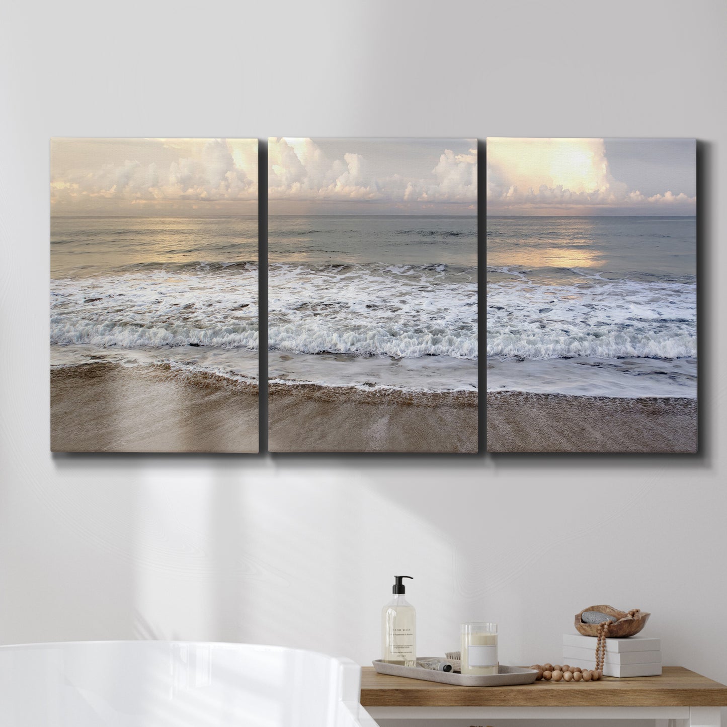 Three-panel canvas wall art featuring calm coastal shoreline seascape, displayed in a bathroom above a bathtub.