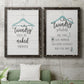 Set of two black barnwood framed canvas prints depicting a coordinated art pair of humorous laundry-room sayings and clothing icons rendered as rustic typographic wall art above a sofa in a modern living room.