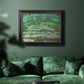 Impressionist garden scene with Japanese bridge and water lilies by Claude Monet in an ornate black frame with gilded inner detail displayed in a dark-toned interior setting.