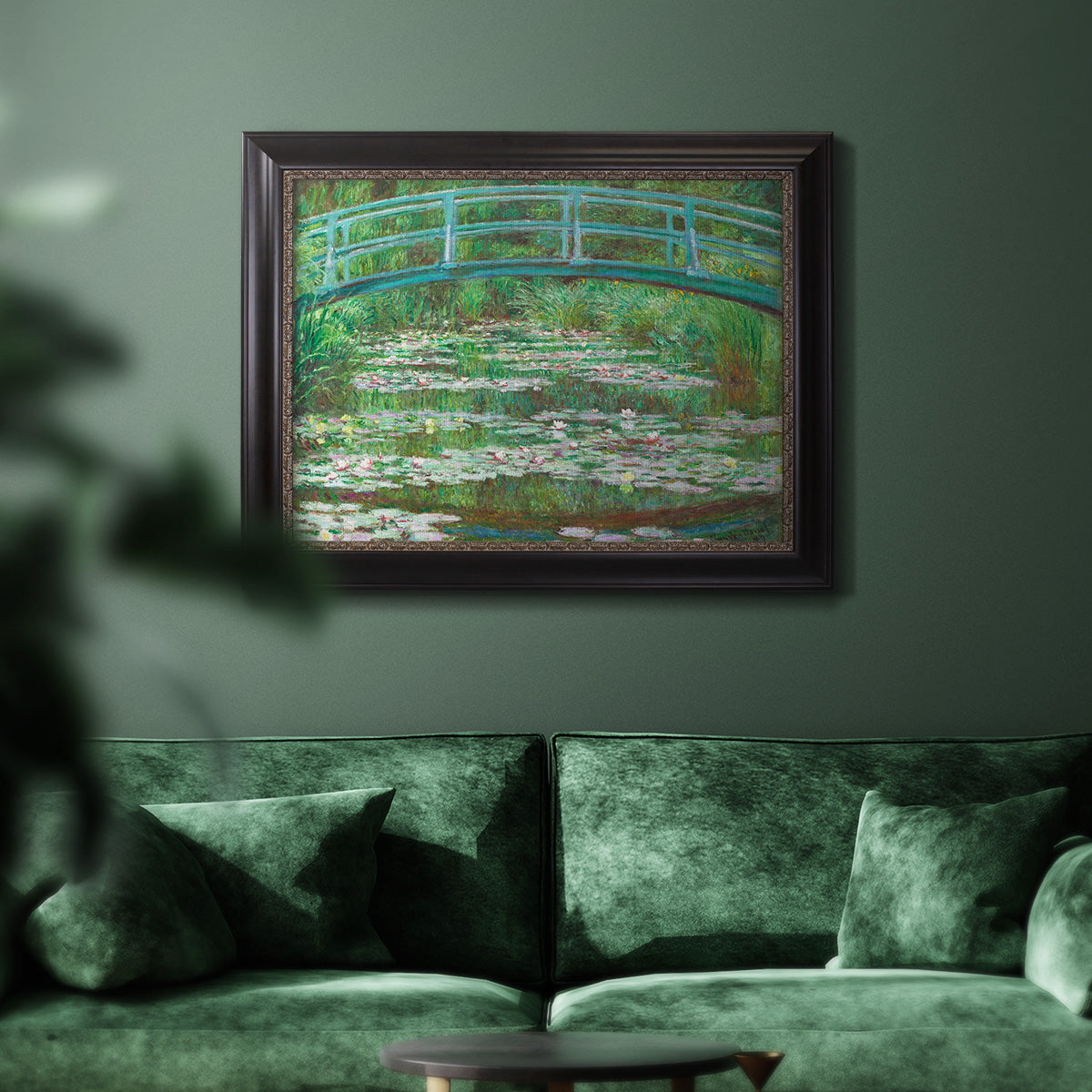 Impressionist garden scene with Japanese bridge and water lilies by Claude Monet in an ornate black frame with gilded inner detail displayed in a dark-toned interior setting.