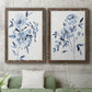 Set of two walnut barnwood framed canvas prints depicting a coordinated art pair of loose blue flowers and leafy branches rendered as expressive watercolor botanical paintings above a sofa in a modern living room.