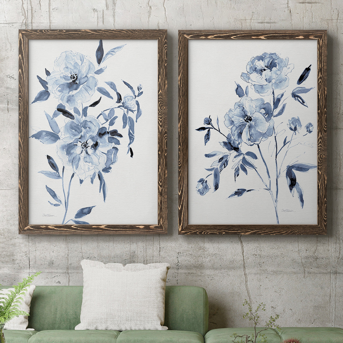 Set of two walnut barnwood framed canvas prints depicting a coordinated art pair of loose blue flowers and leafy branches rendered as expressive watercolor botanical paintings above a sofa in a modern living room.