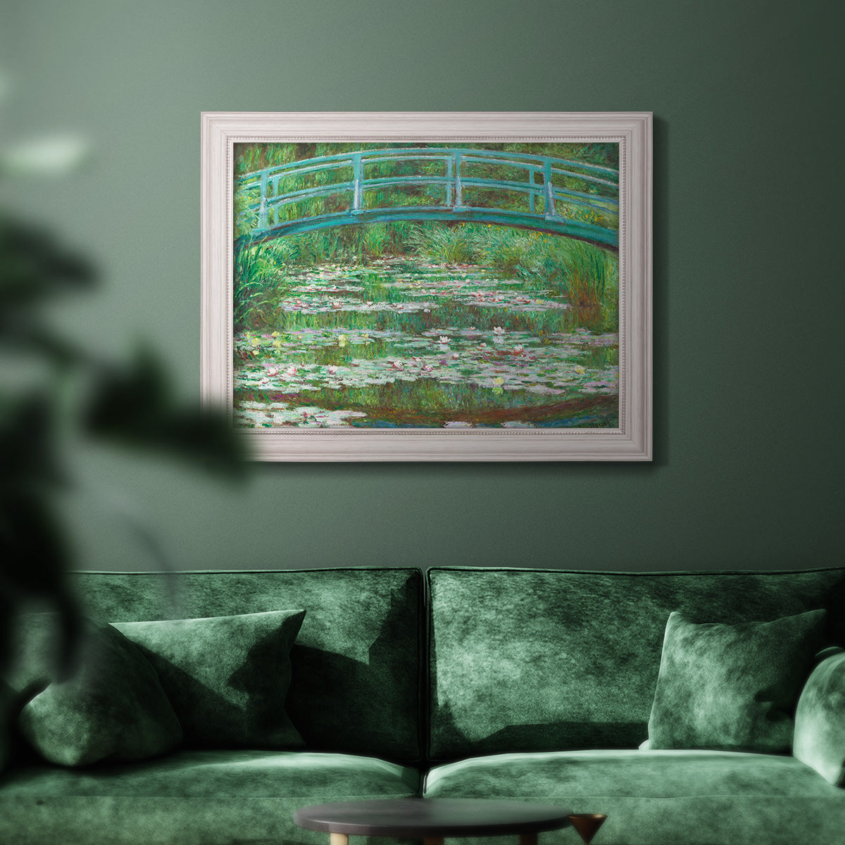 Impressionist garden scene with Japanese bridge and water lilies by Claude Monet in an ornate weathered white frame displayed in a dark-toned interior setting.