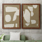 Set of two maple barnwood framed canvas prints depicting a coordinated art pair of irregular white cutout-like shapes on taupe grounds rendered as bold minimalist shape abstracts above a sofa in a modern living room.