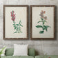 Set of two walnut barnwood framed canvas prints depicting antique floral illustrations featuring a tall red bloom and a clustered mauve flower above a sofa in a modern living room.