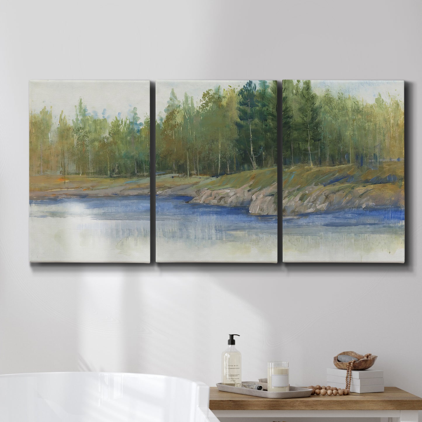 Three-panel canvas wall art featuring riverbank landscape with trees, displayed in a bathroom above a bathtub.