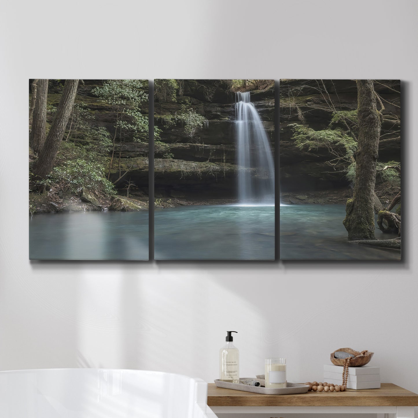 Three-panel canvas wall art featuring waterfall cascading through forest, displayed in a bathroom above a bathtub.