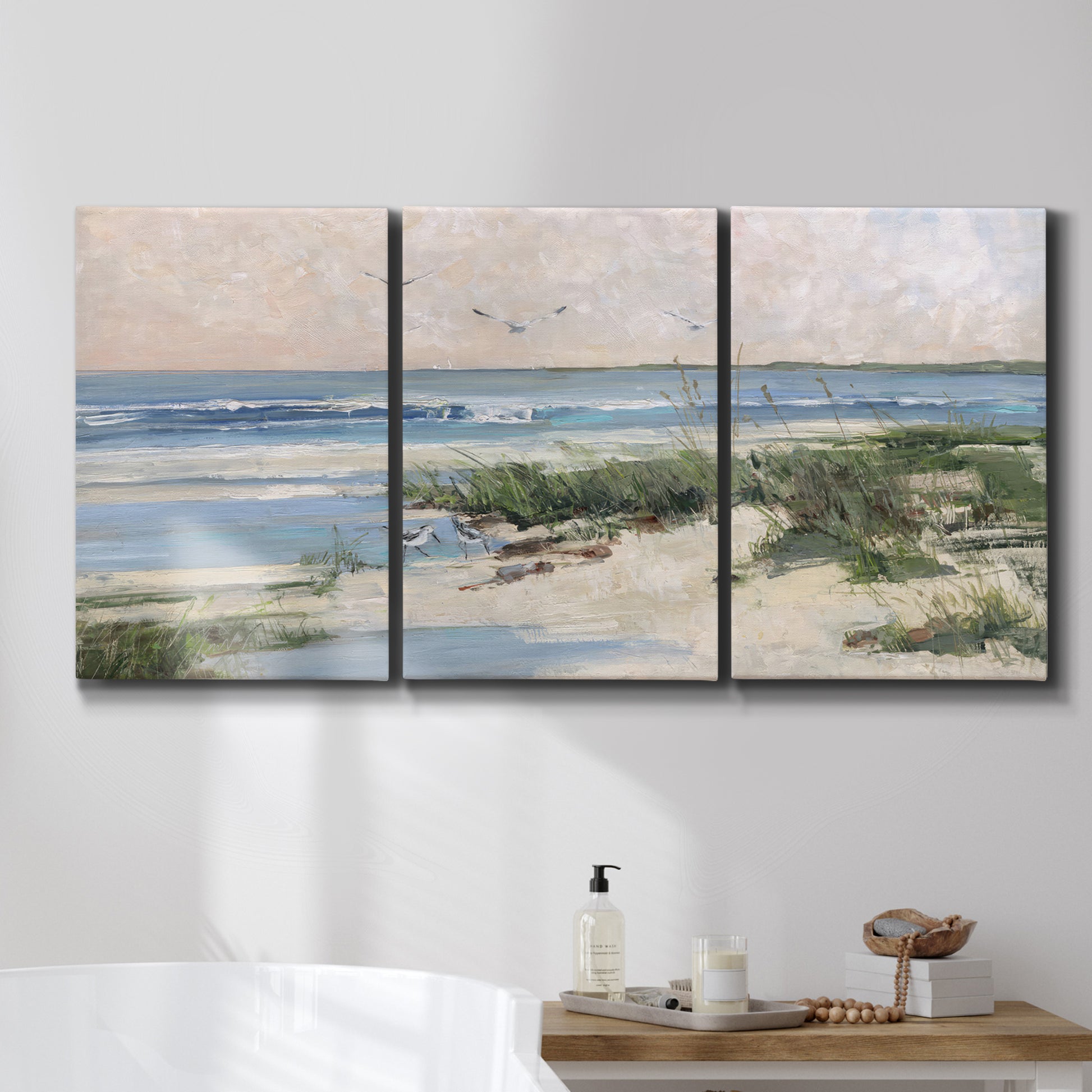 Three-panel canvas wall art featuring soft morning light over calm sea, displayed in a bathroom above a bathtub.