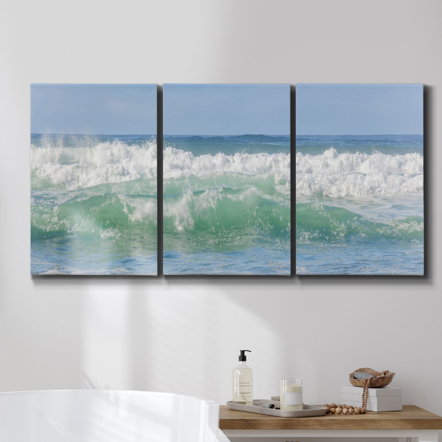 Three-panel canvas wall art featuring coastal waves breaking ashore, displayed in a bathroom above a bathtub.