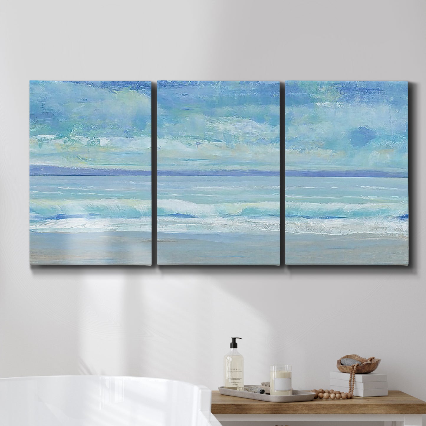 Three-panel canvas wall art featuring rolling ocean surf along shoreline, displayed in a bathroom above a bathtub.
