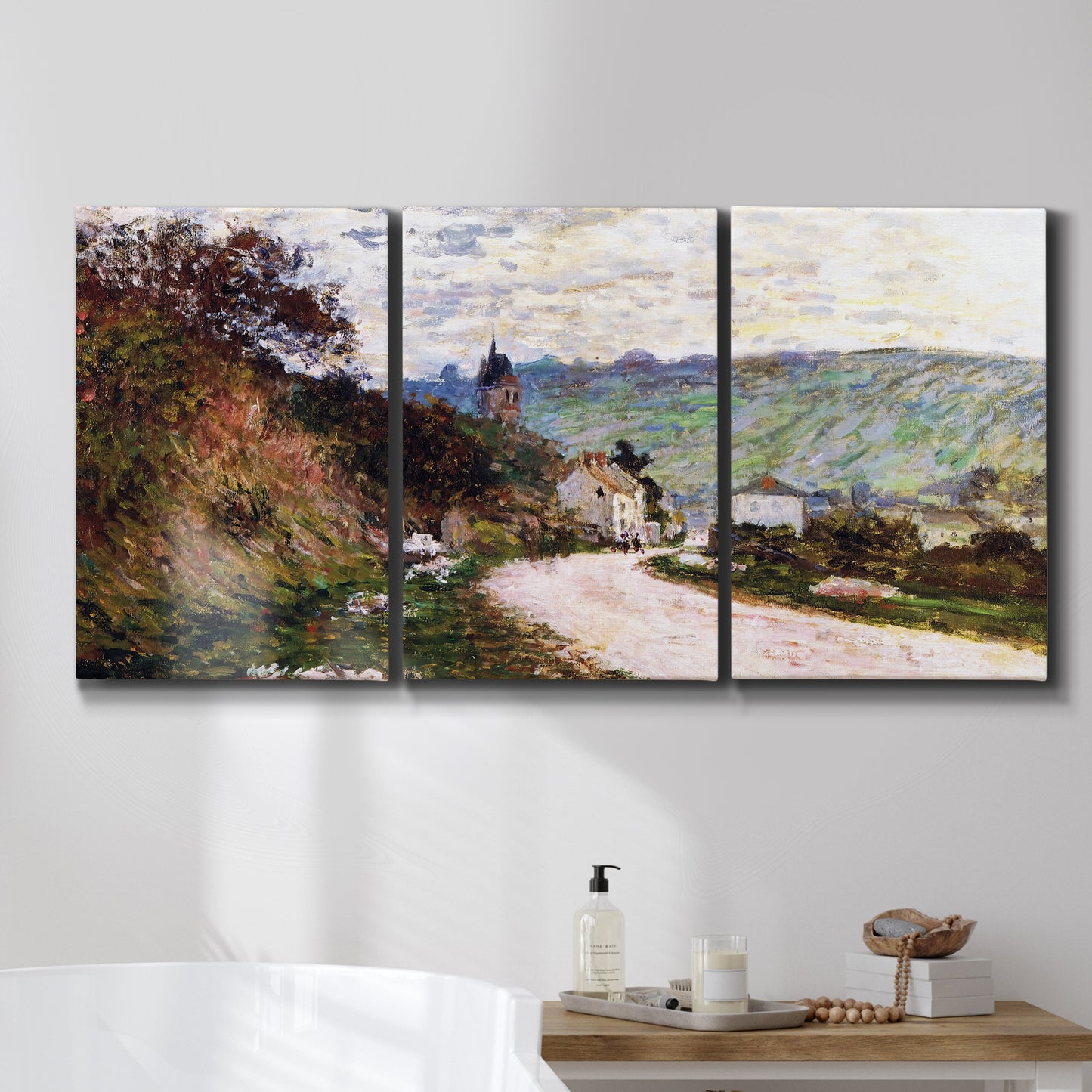 Three-panel canvas wall art featuring country road through village, displayed in a bathroom above a bathtub.