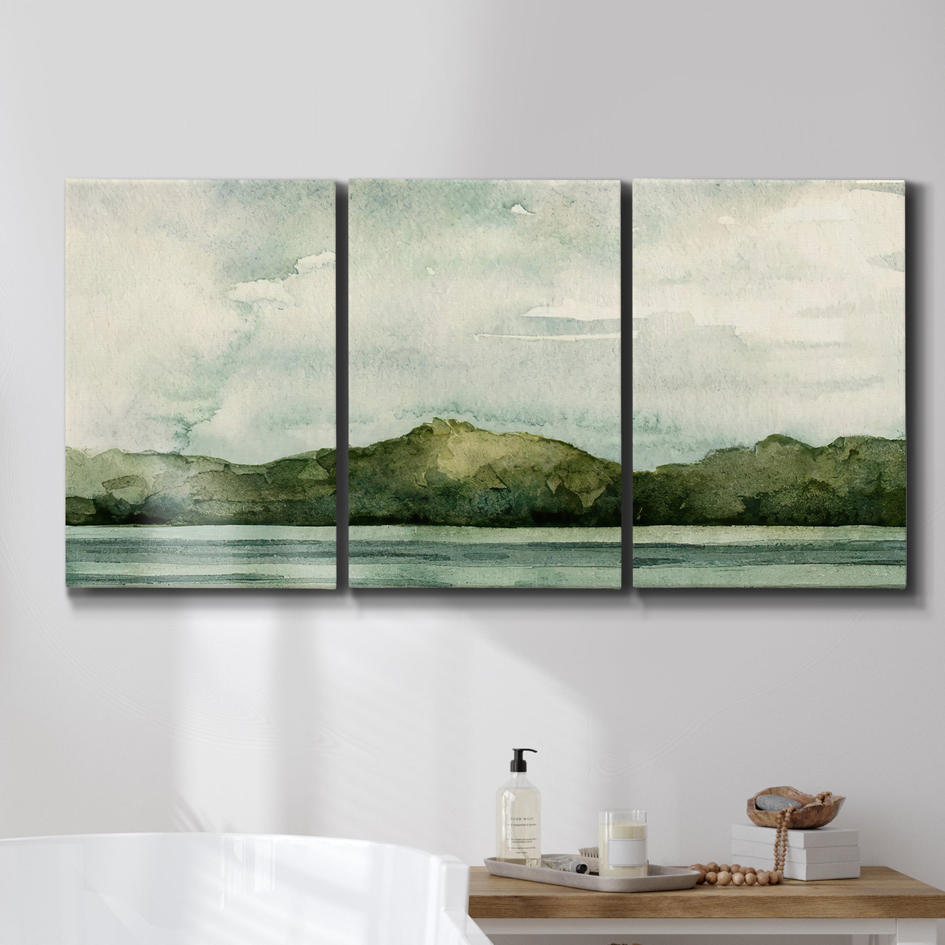 Three-panel canvas wall art featuring riverbank watercolor landscape, displayed in a bathroom above a bathtub.