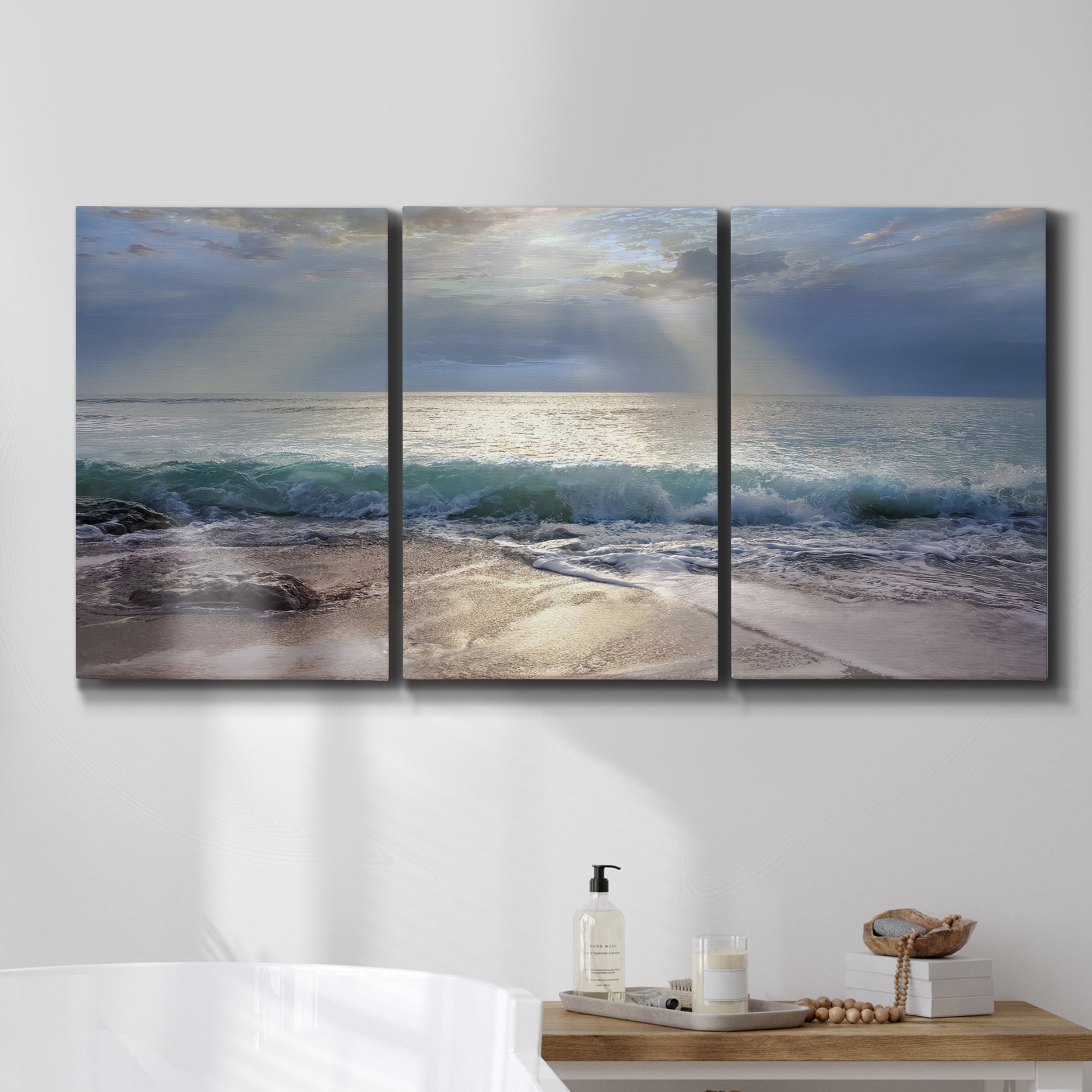 Three-panel canvas wall art featuring soft sunrise over open water, displayed in a bathroom above a bathtub.