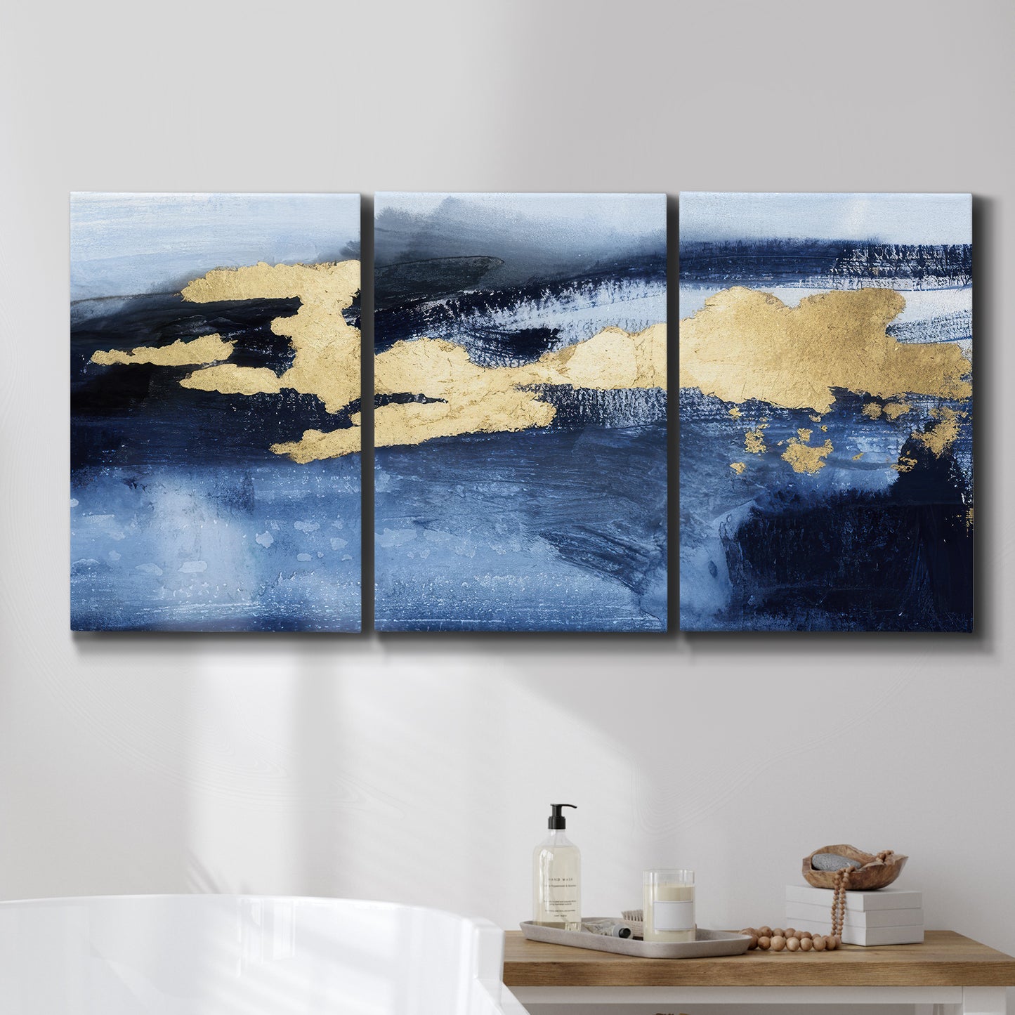 Three-panel canvas wall art featuring coastal shoreline with warm light, displayed in a bathroom above a bathtub.