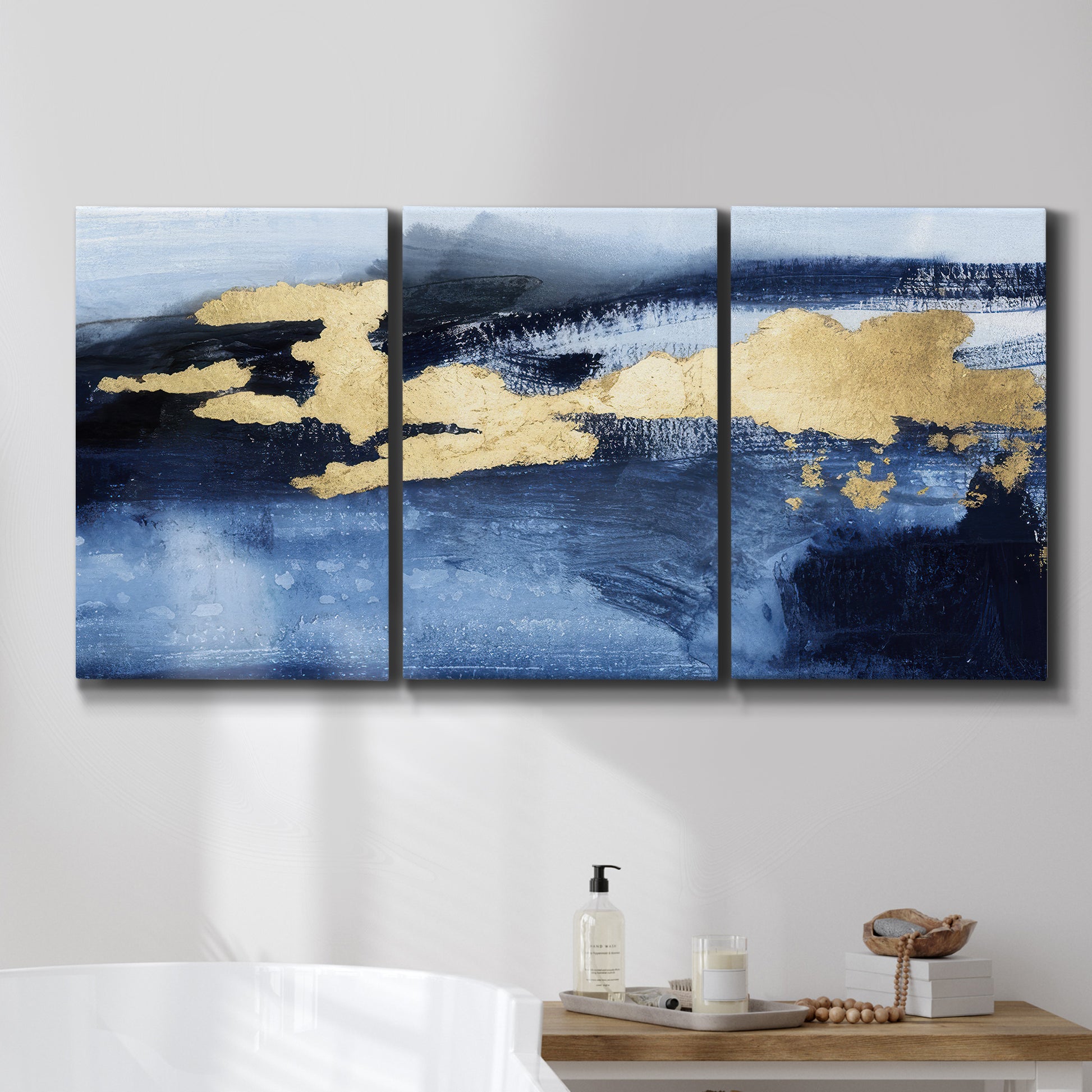 Three-panel canvas wall art featuring coastal shoreline with warm light, displayed in a bathroom above a bathtub.