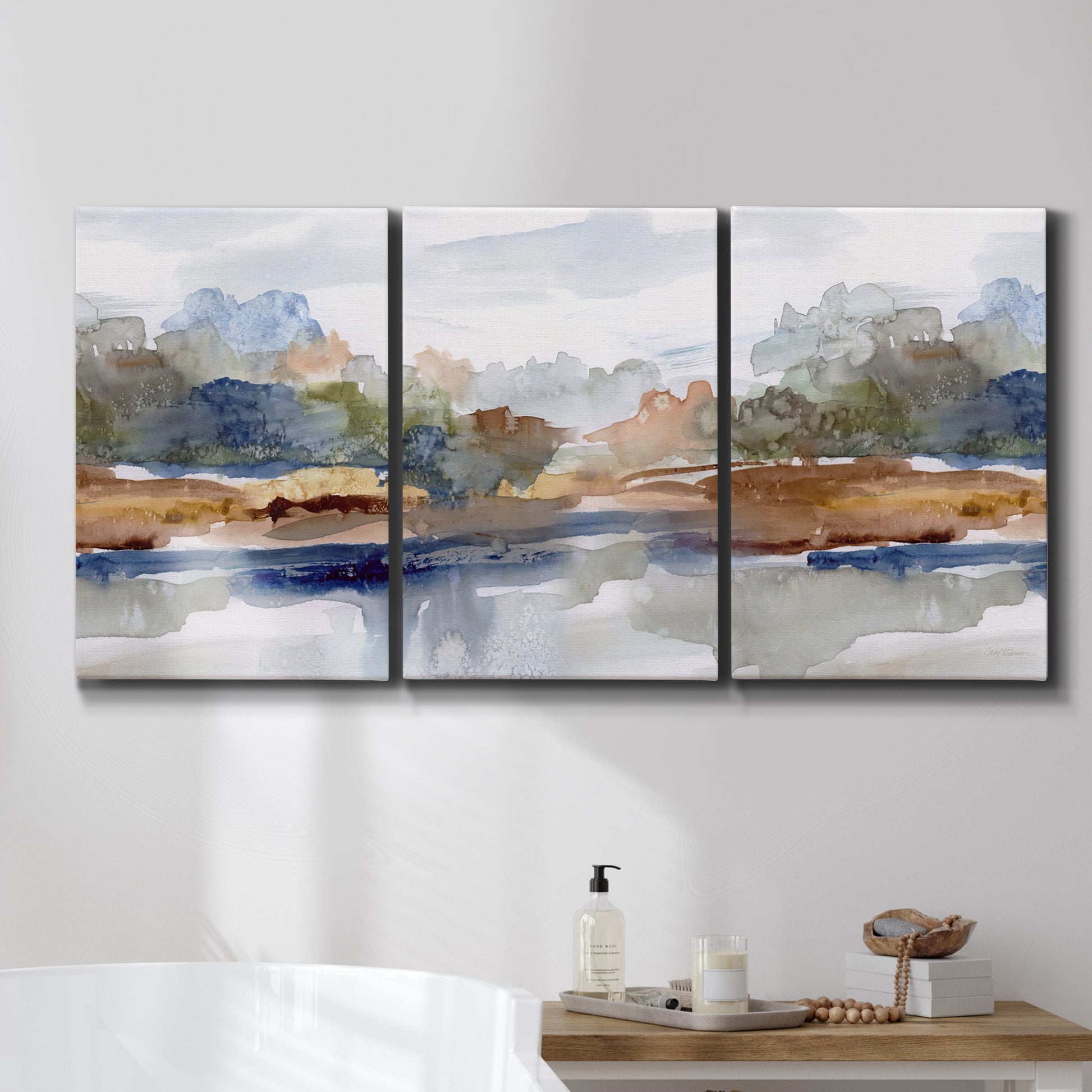 Three-panel canvas wall art featuring layered abstract mountain forms, displayed in a bathroom above a bathtub.