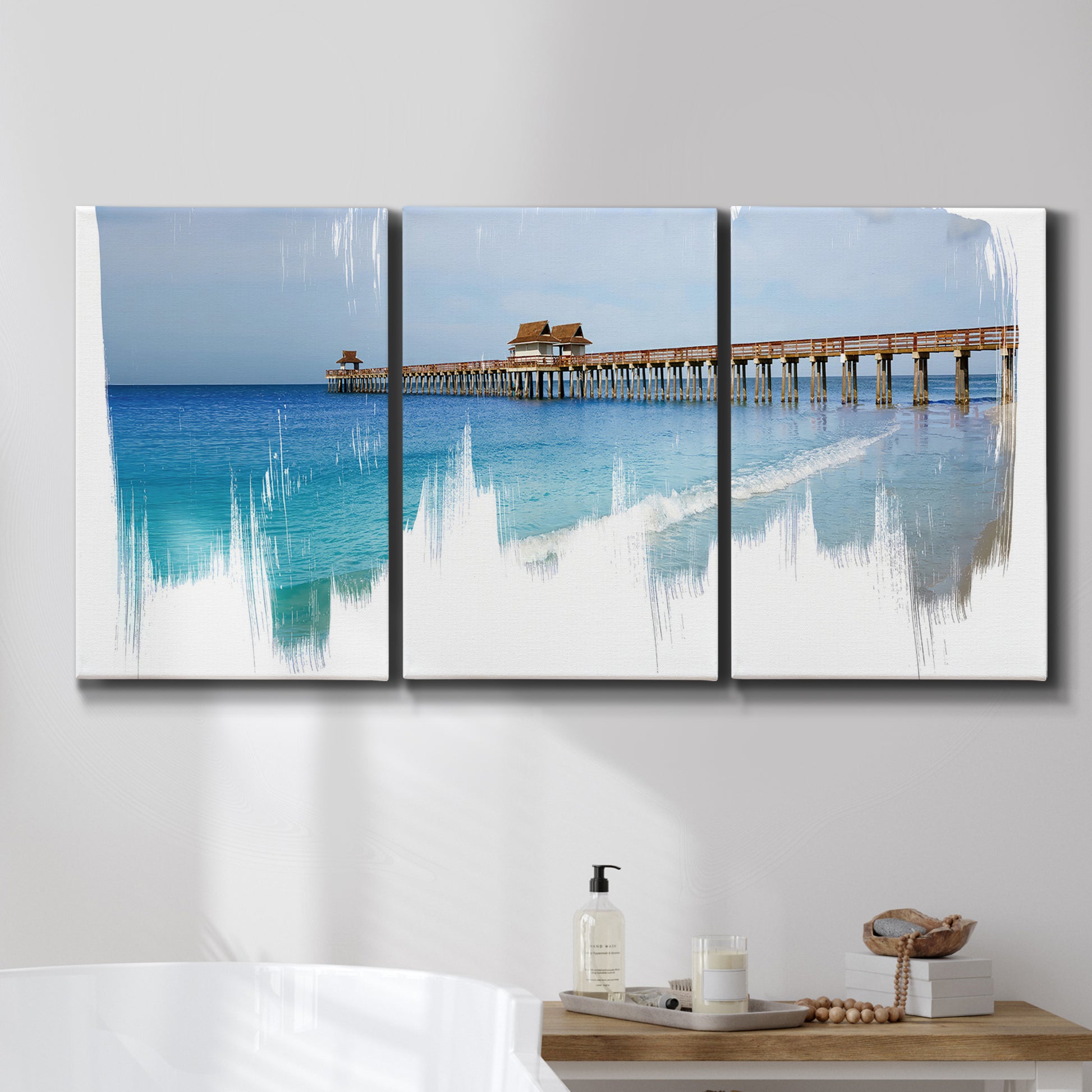 Three-panel canvas wall art featuring coastal pier extending over water, displayed in a bathroom above a bathtub.