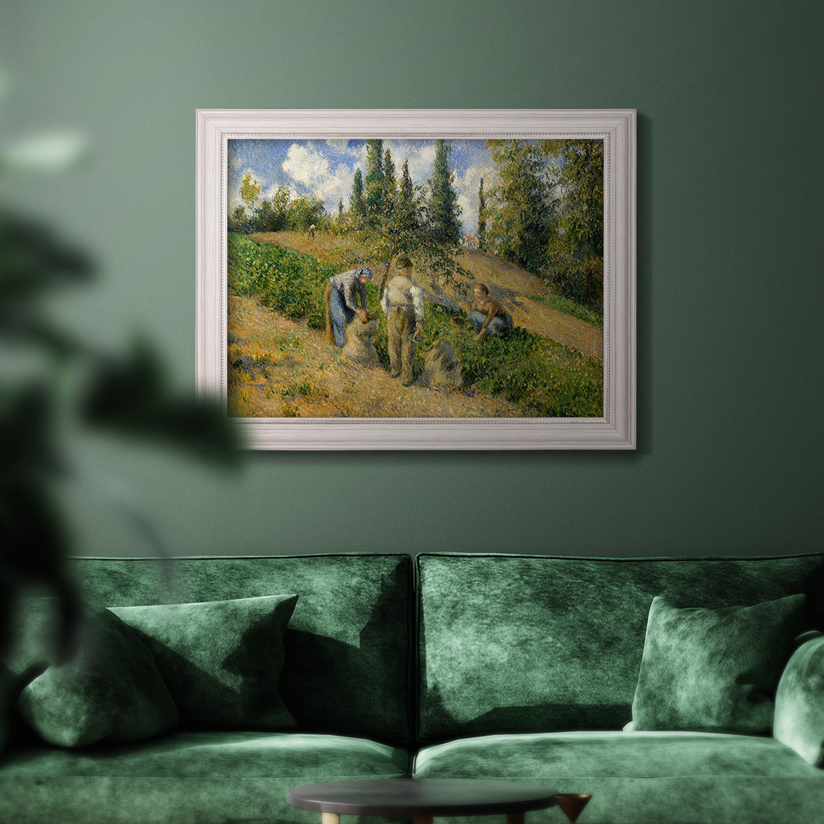 Impressionist countryside harvest scene by Camille Pissarro in an ornate weathered white frame displayed in a dark-toned interior setting.