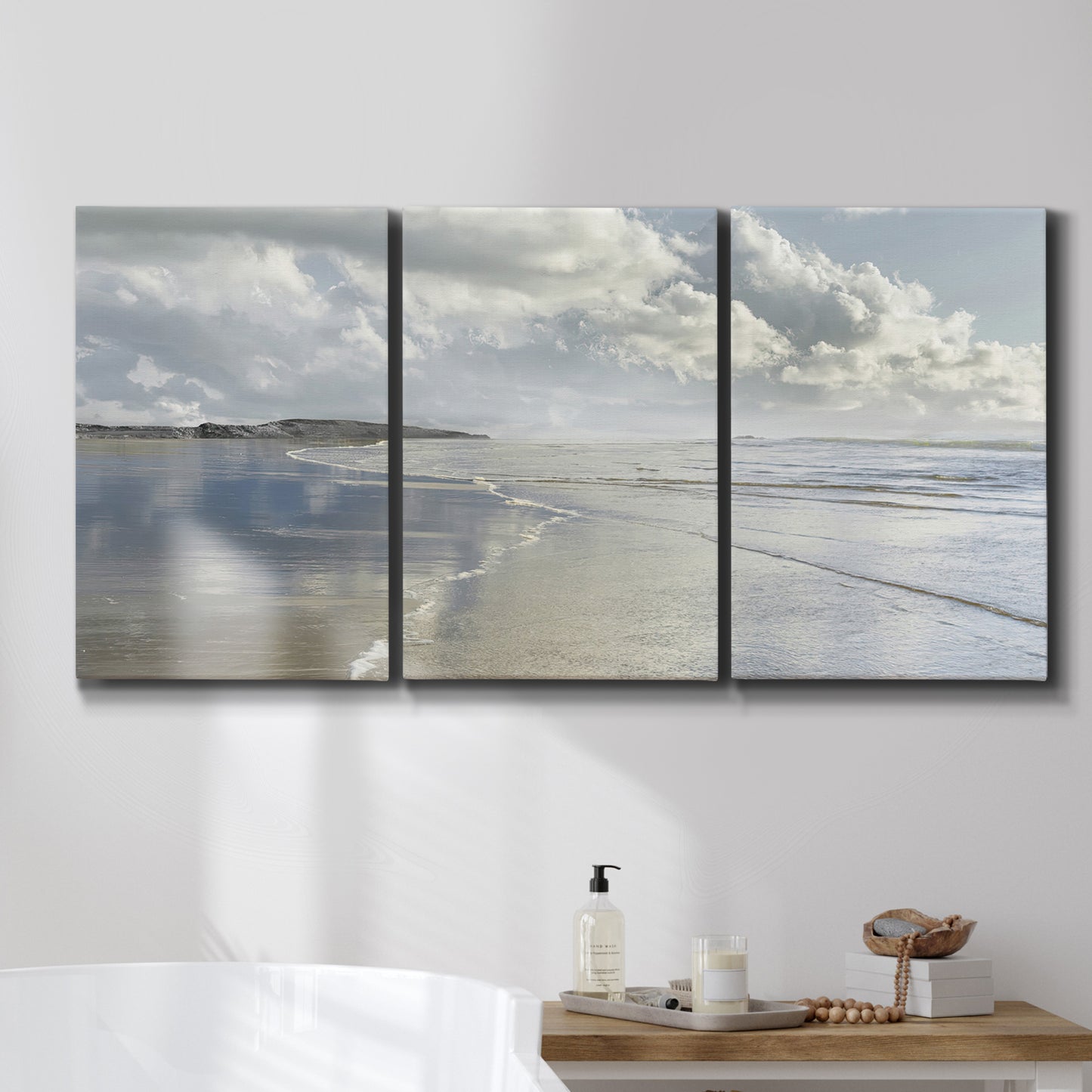 Three-panel canvas wall art featuring endless beach meeting ocean horizon, displayed in a bathroom above a bathtub.