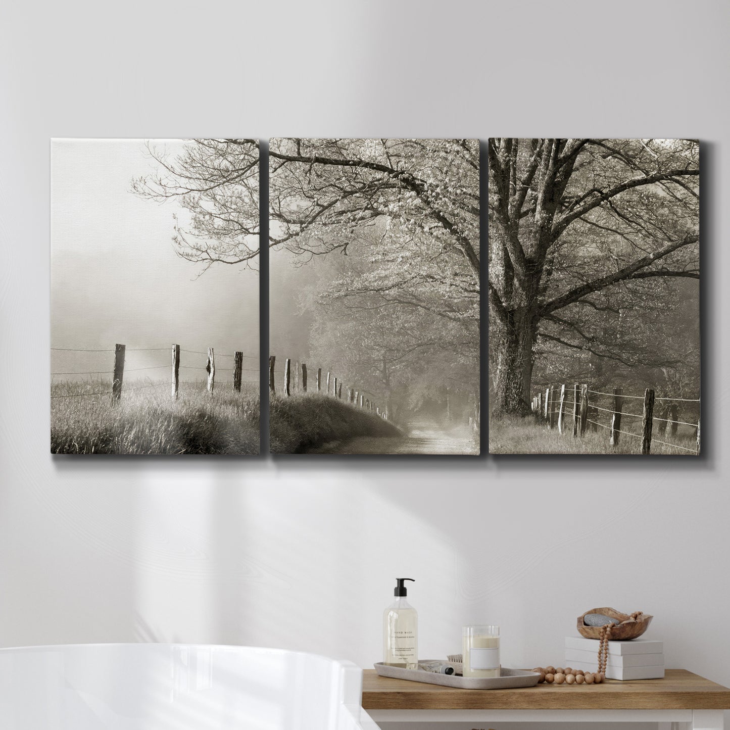 Three-panel canvas wall art featuring fenced rural path through countryside, displayed in a bathroom above a bathtub.