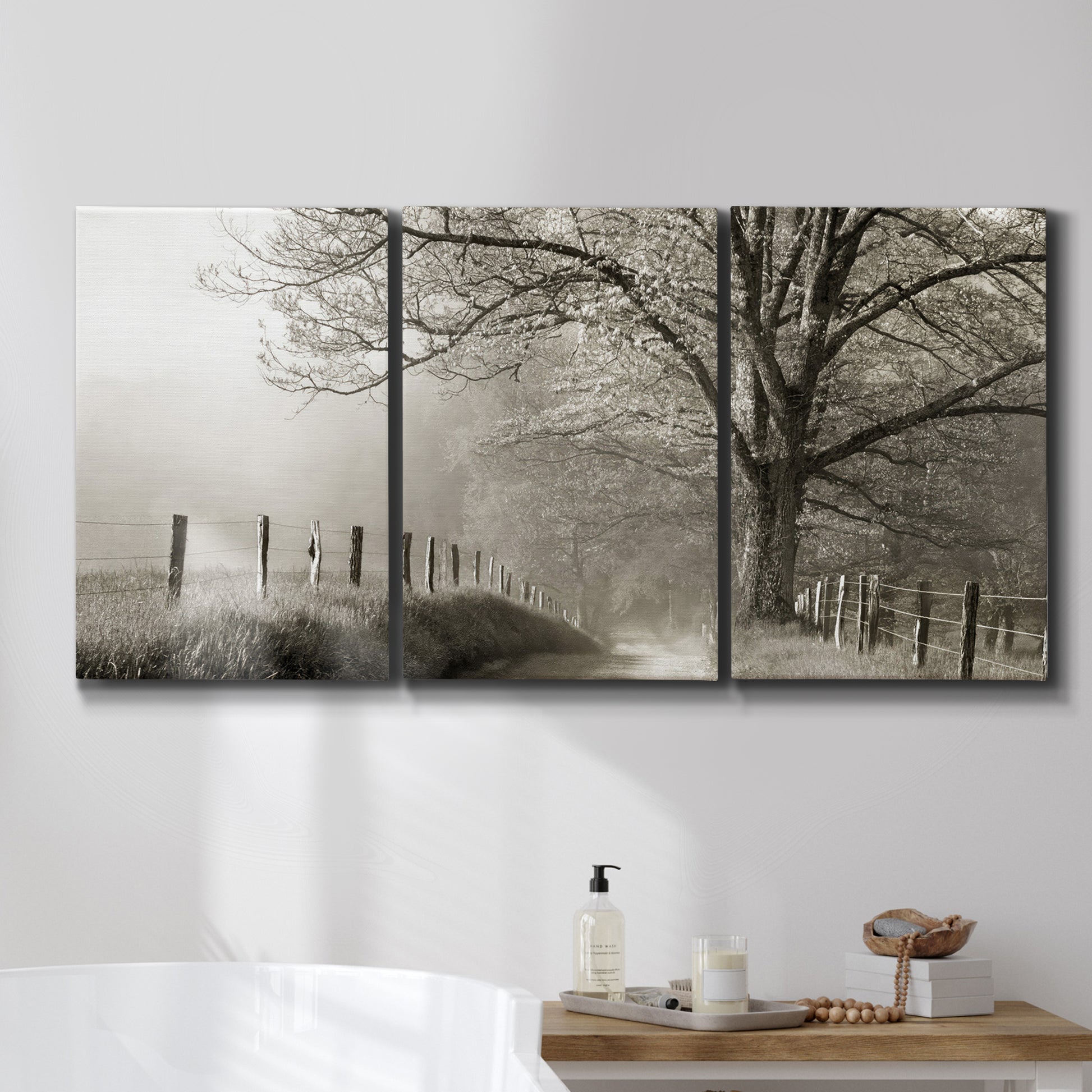 Three-panel canvas wall art featuring fenced rural path through countryside, displayed in a bathroom above a bathtub.