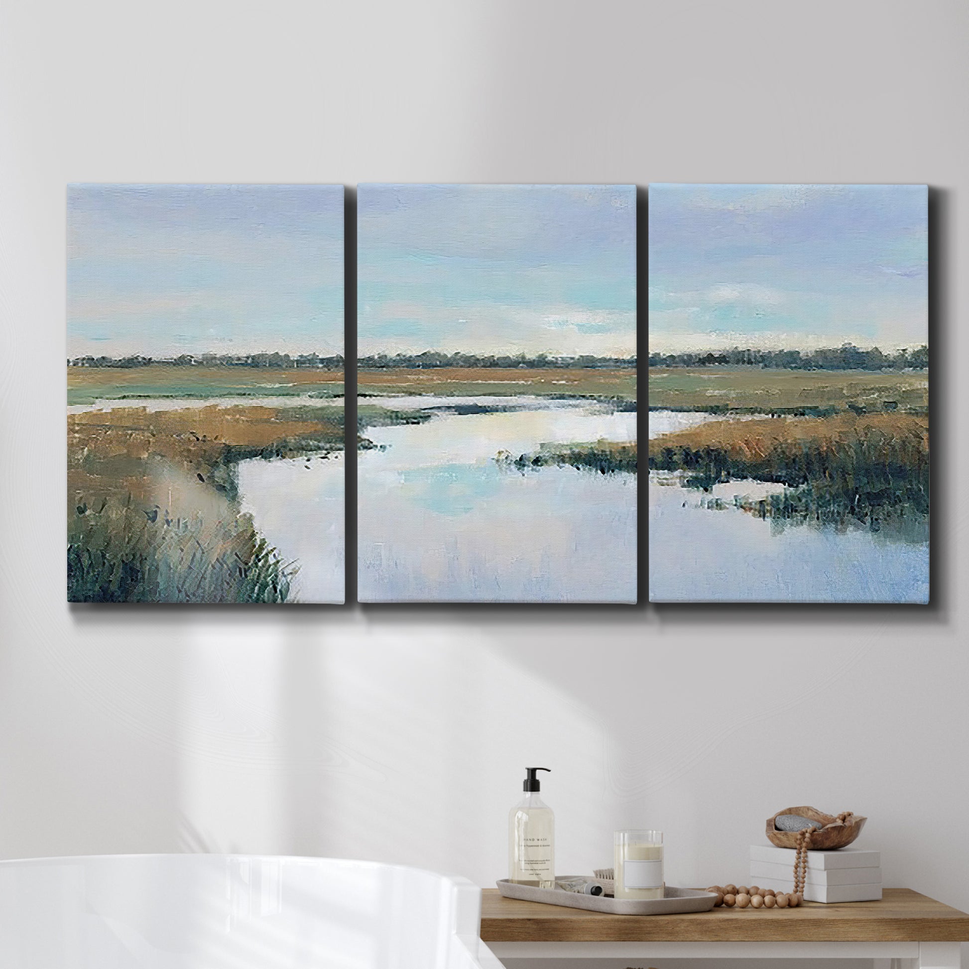 Three-panel canvas wall art featuring coastal plain meeting open water, displayed in a bathroom above a bathtub.