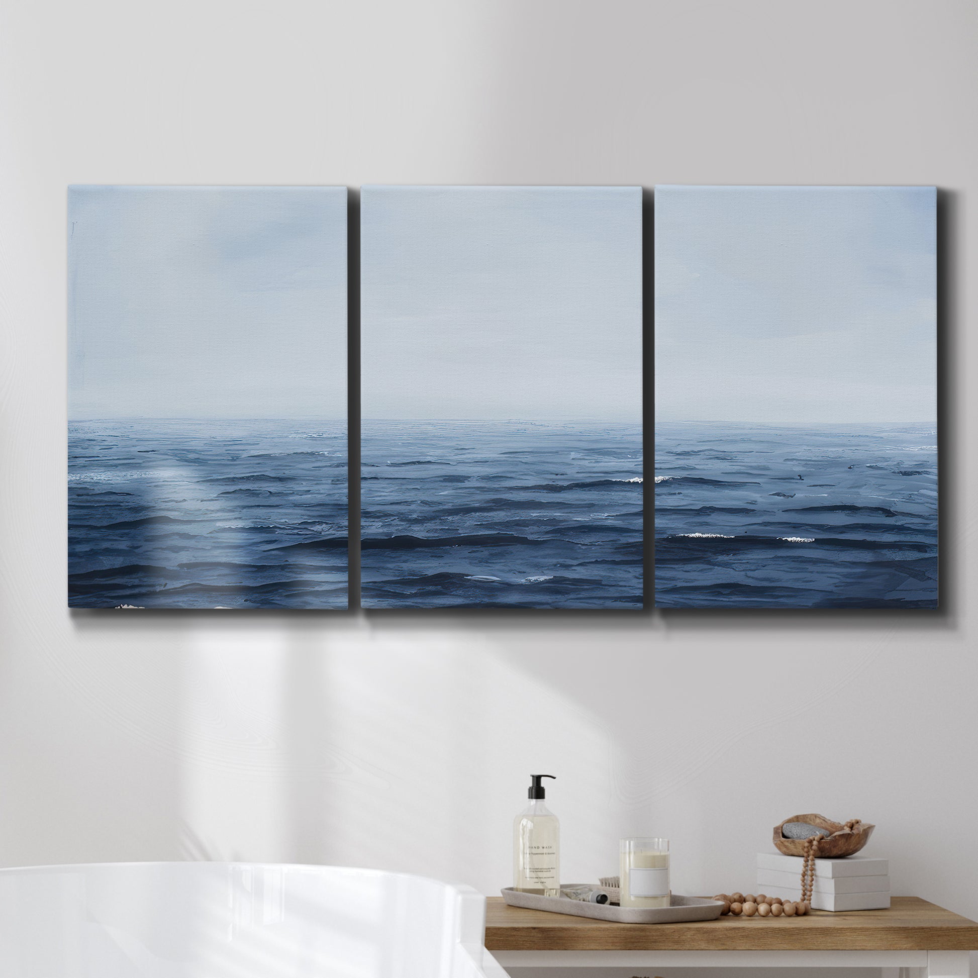 Three-panel canvas wall art featuring grayscale seascape with horizon, displayed in a bathroom above a bathtub.