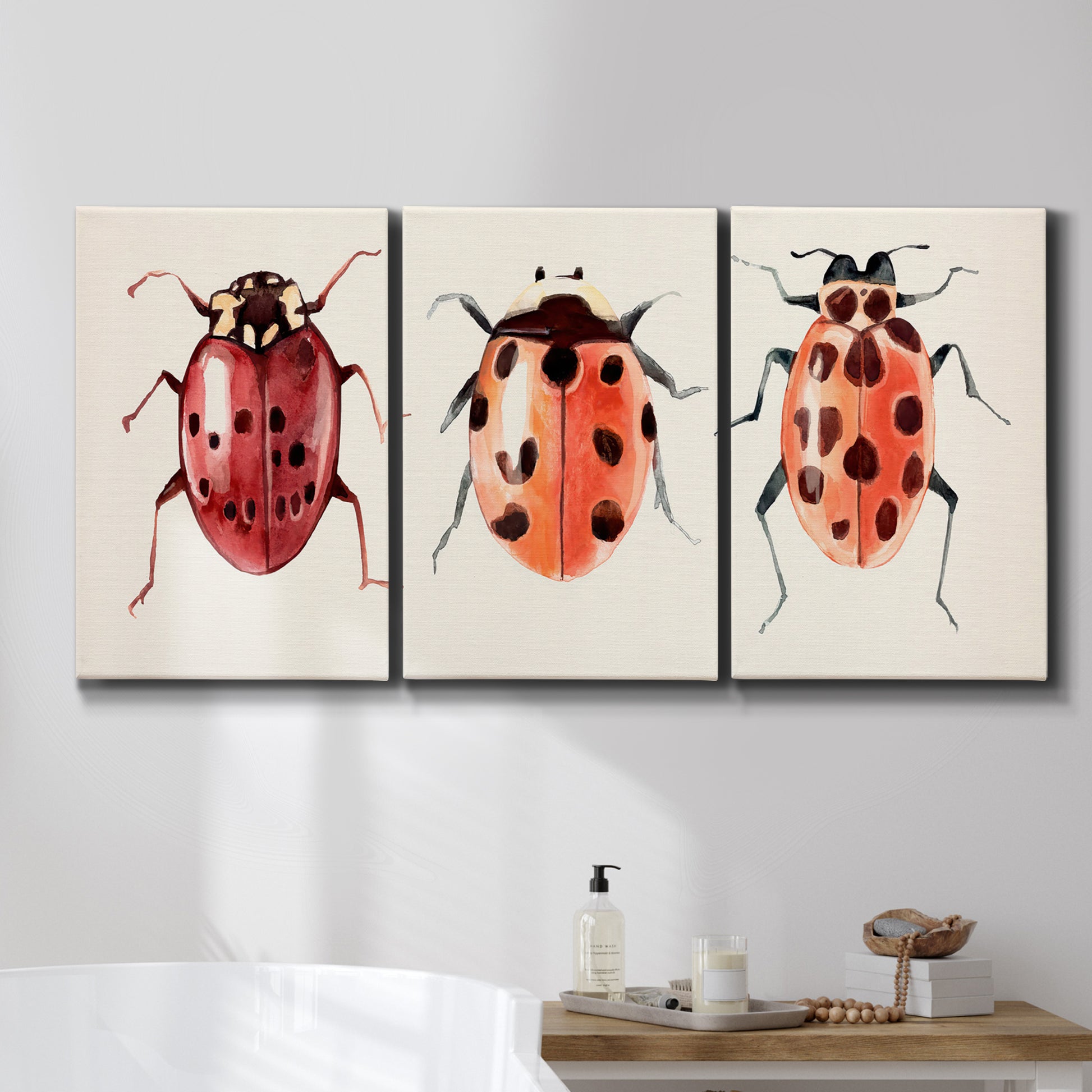 Three-panel canvas wall art featuring ladybugs on green foliage, displayed in a bathroom above a bathtub.