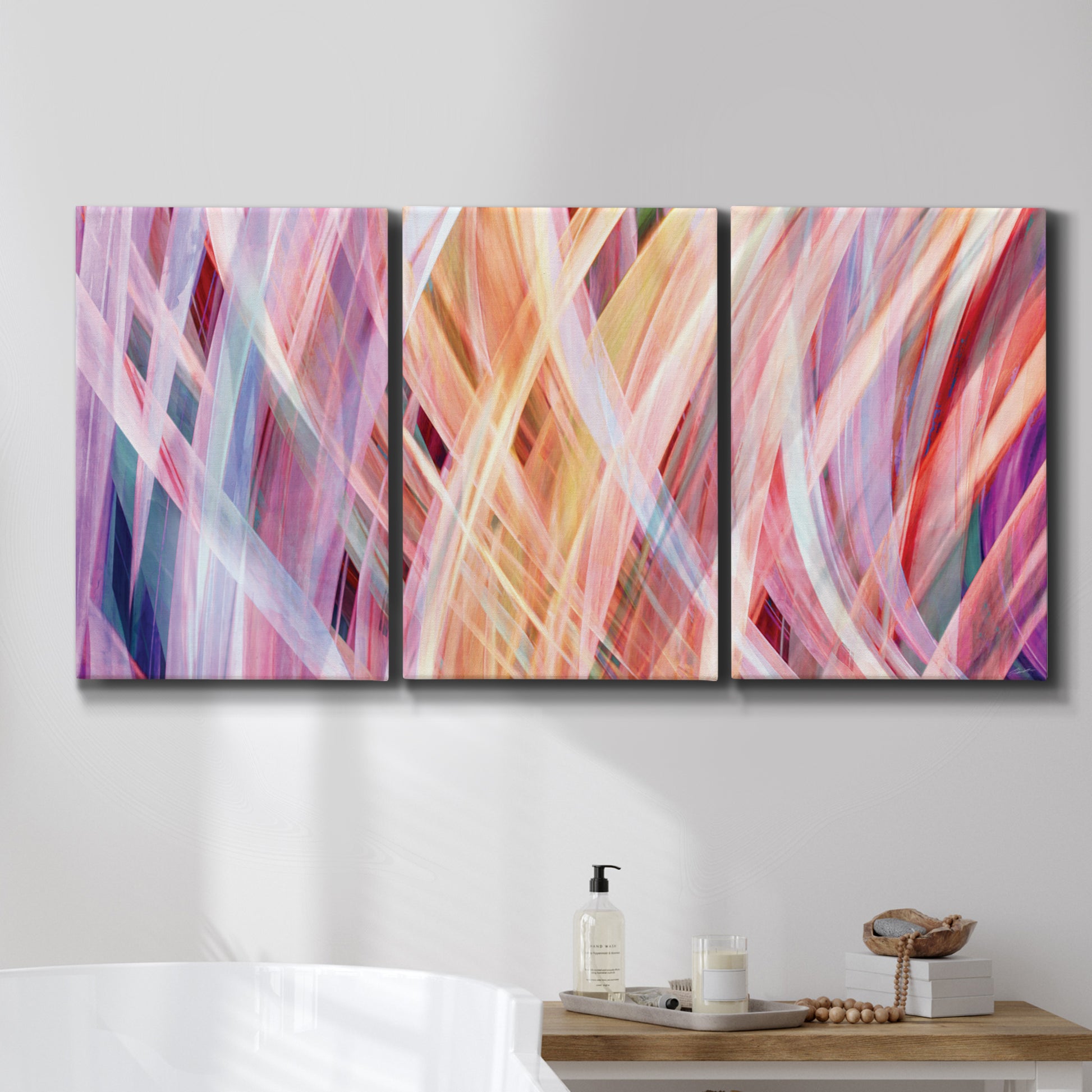 Three-panel canvas wall art featuring layered modern abstract color ribbons, displayed in a bathroom above a bathtub.