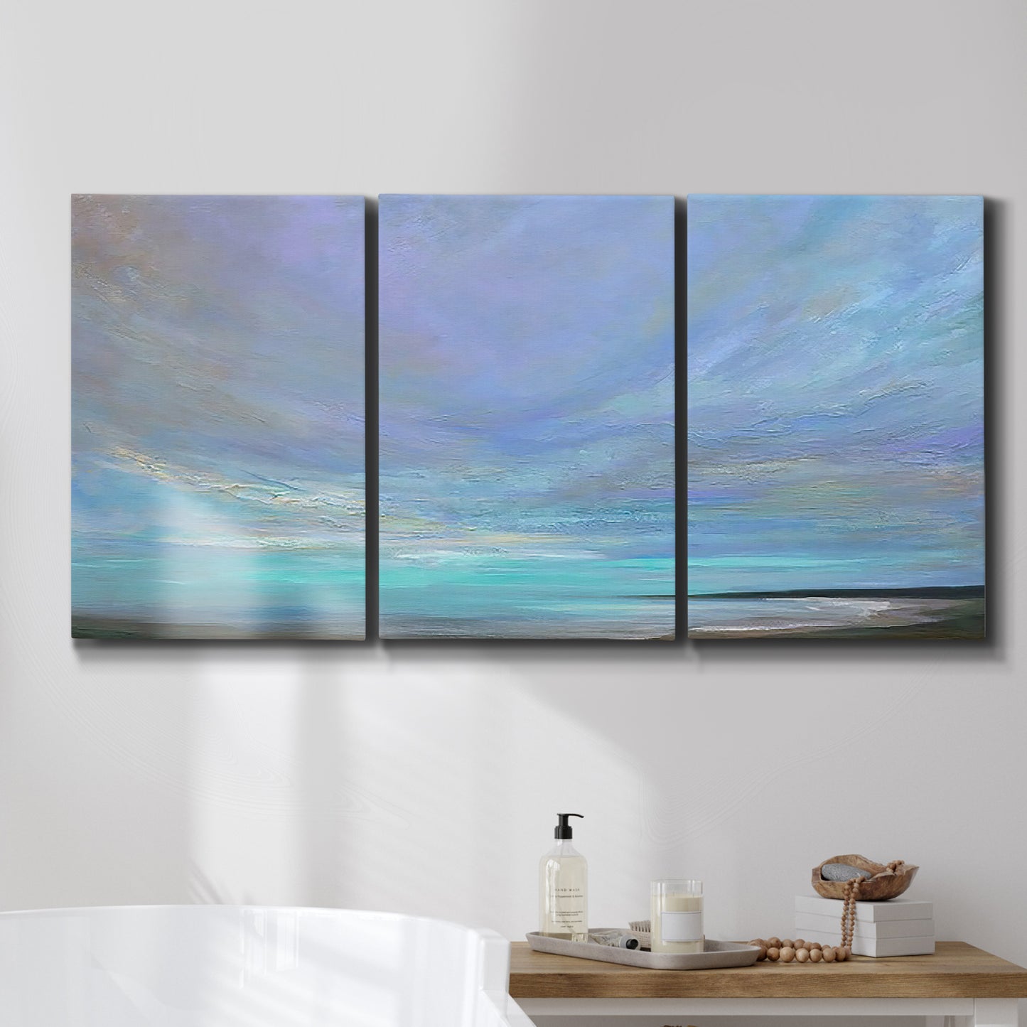 Three-panel canvas wall art featuring coastal shoreline with gentle surf, displayed in a bathroom above a bathtub.