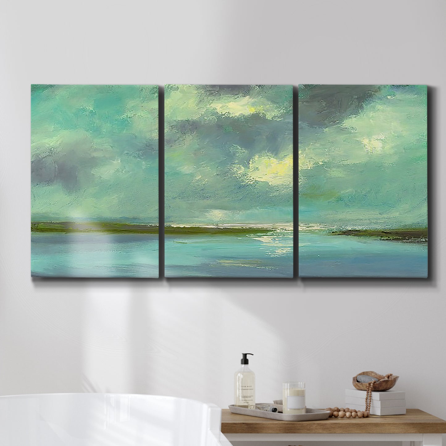 Three-panel canvas wall art featuring still lagoon water beneath open sky, displayed in a bathroom above a bathtub.