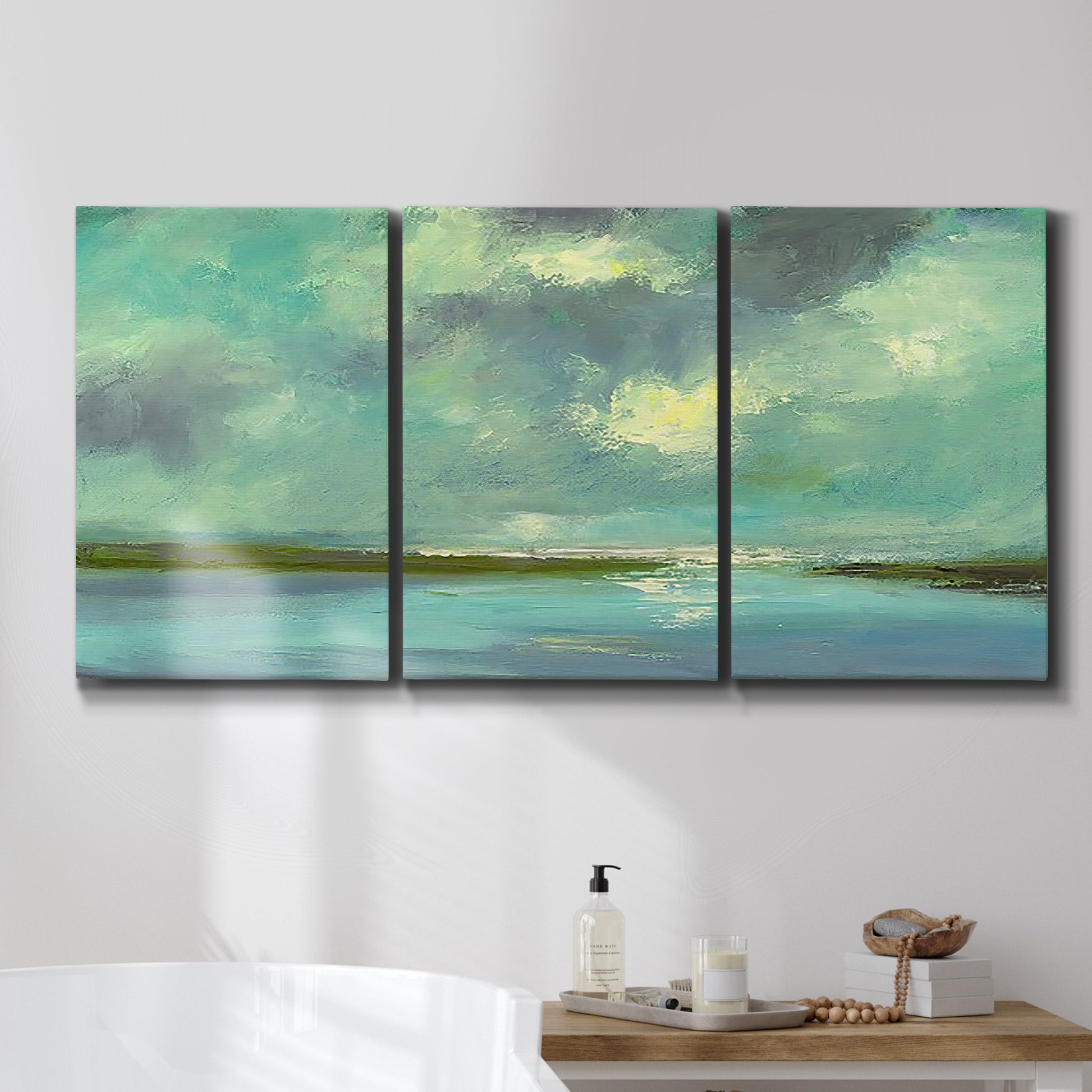 Three-panel canvas wall art featuring still lagoon water beneath open sky, displayed in a bathroom above a bathtub.
