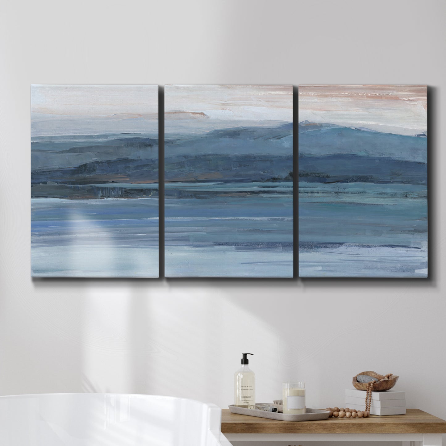 Three-panel canvas wall art featuring wide lake with distant shoreline, displayed in a bathroom above a bathtub.