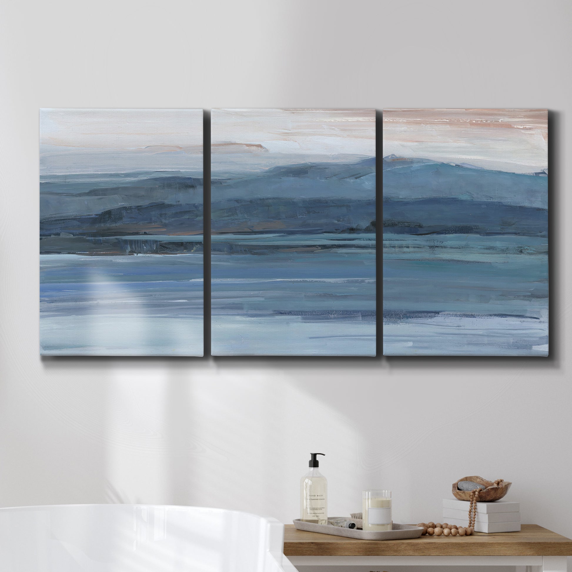 Three-panel canvas wall art featuring wide lake with distant shoreline, displayed in a bathroom above a bathtub.