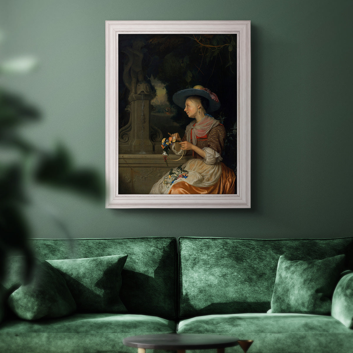 Classical interior scene of a woman weaving flowers by Godfried Schalcken in an ornate weathered white frame displayed in a dark-toned interior setting.