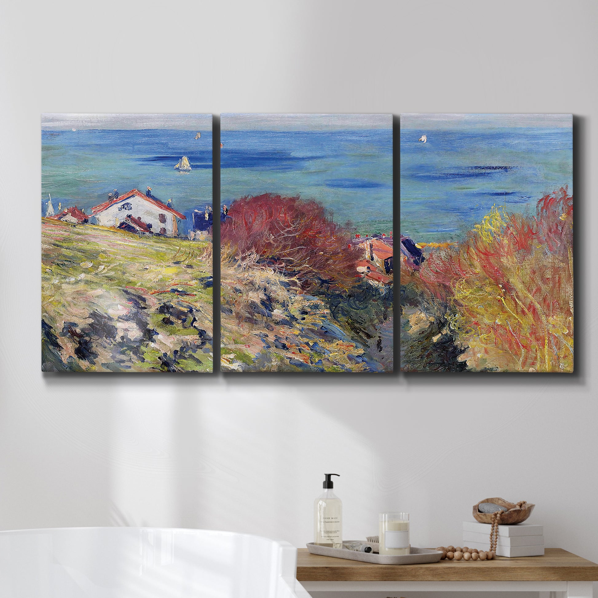 Three-panel canvas wall art featuring coastal village shoreline landscape, displayed in a bathroom above a bathtub.