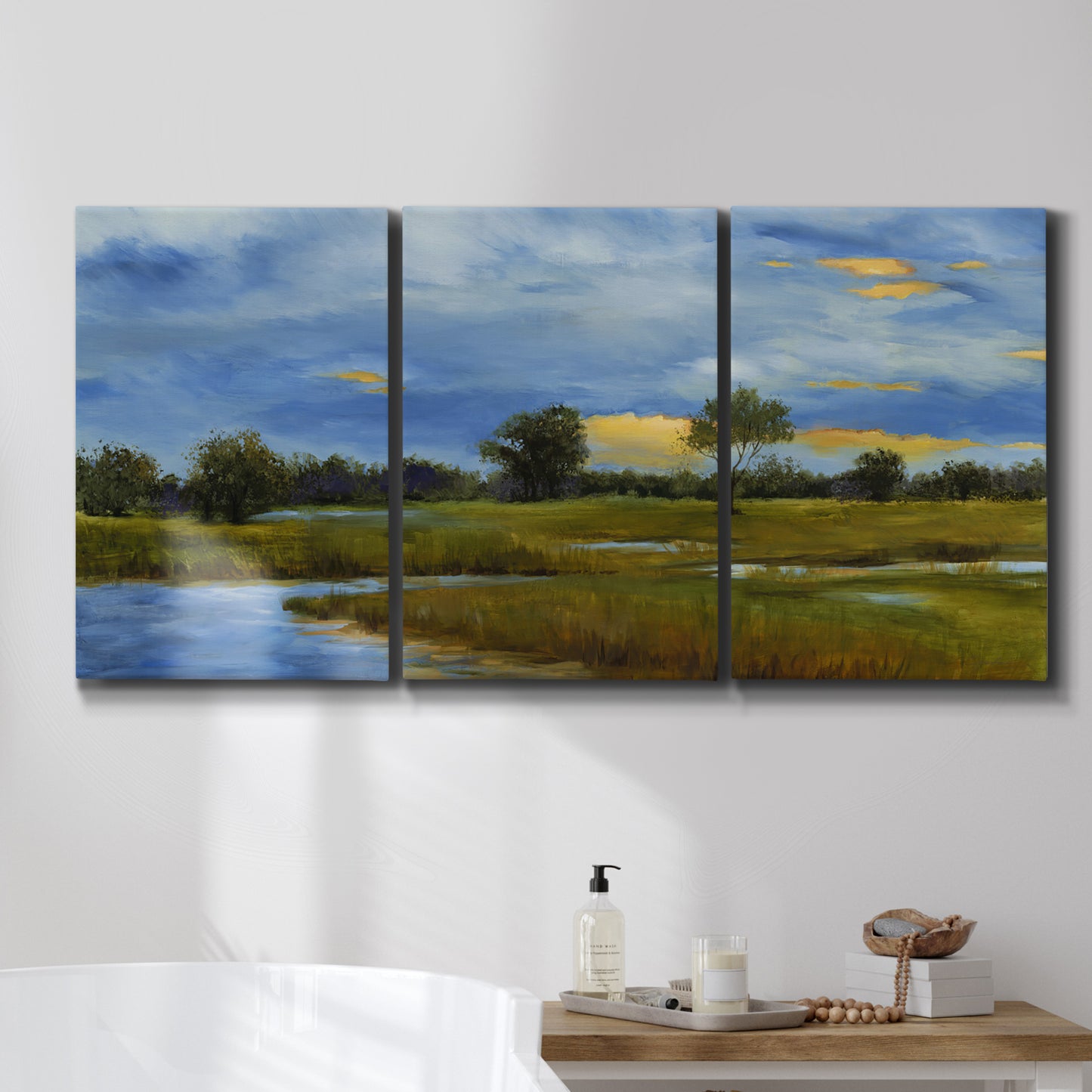 Three-panel canvas wall art featuring riverside walking path through greenery, displayed in a bathroom above a bathtub.