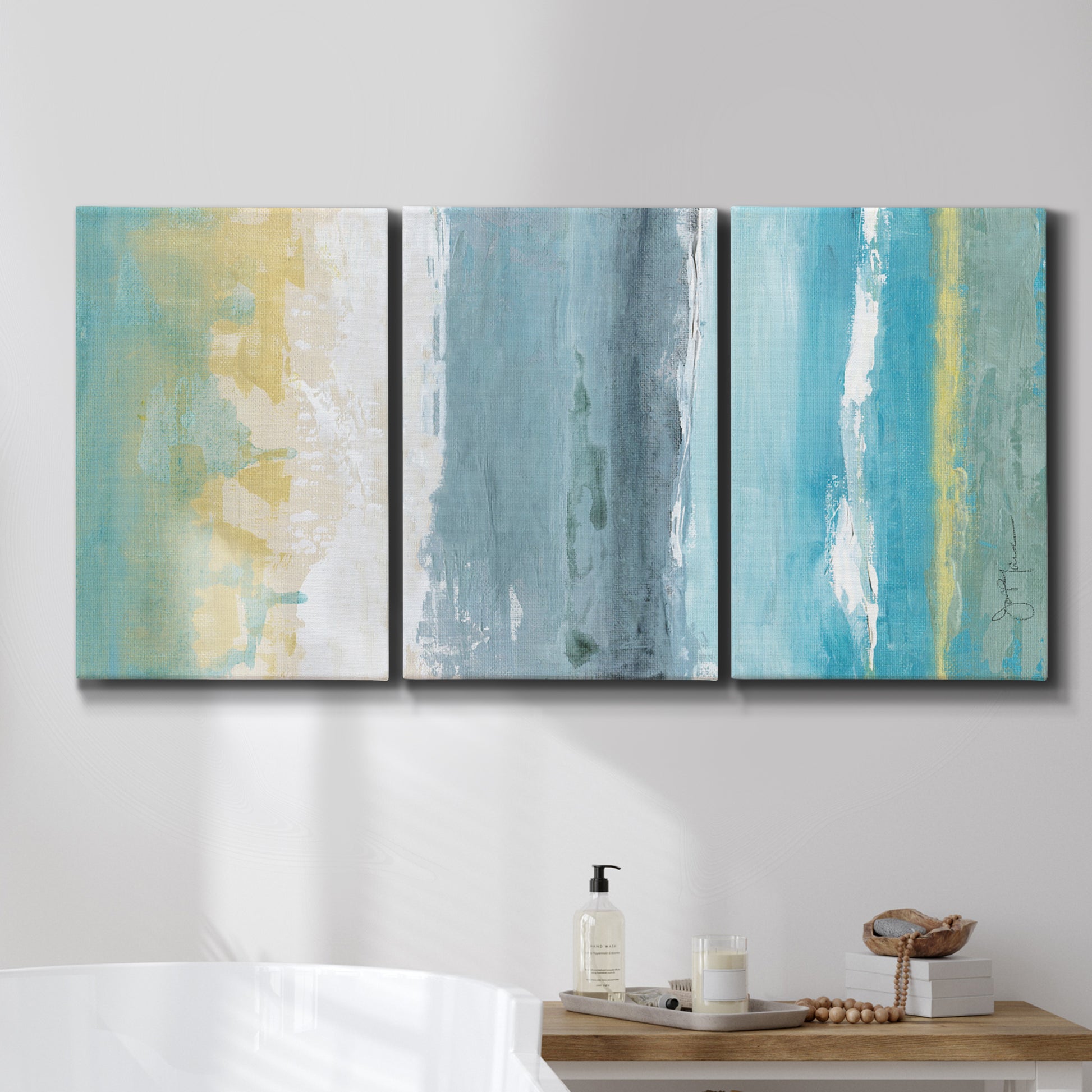 Three-panel canvas wall art featuring abstract coastal beach textures, displayed in a bathroom above a bathtub.