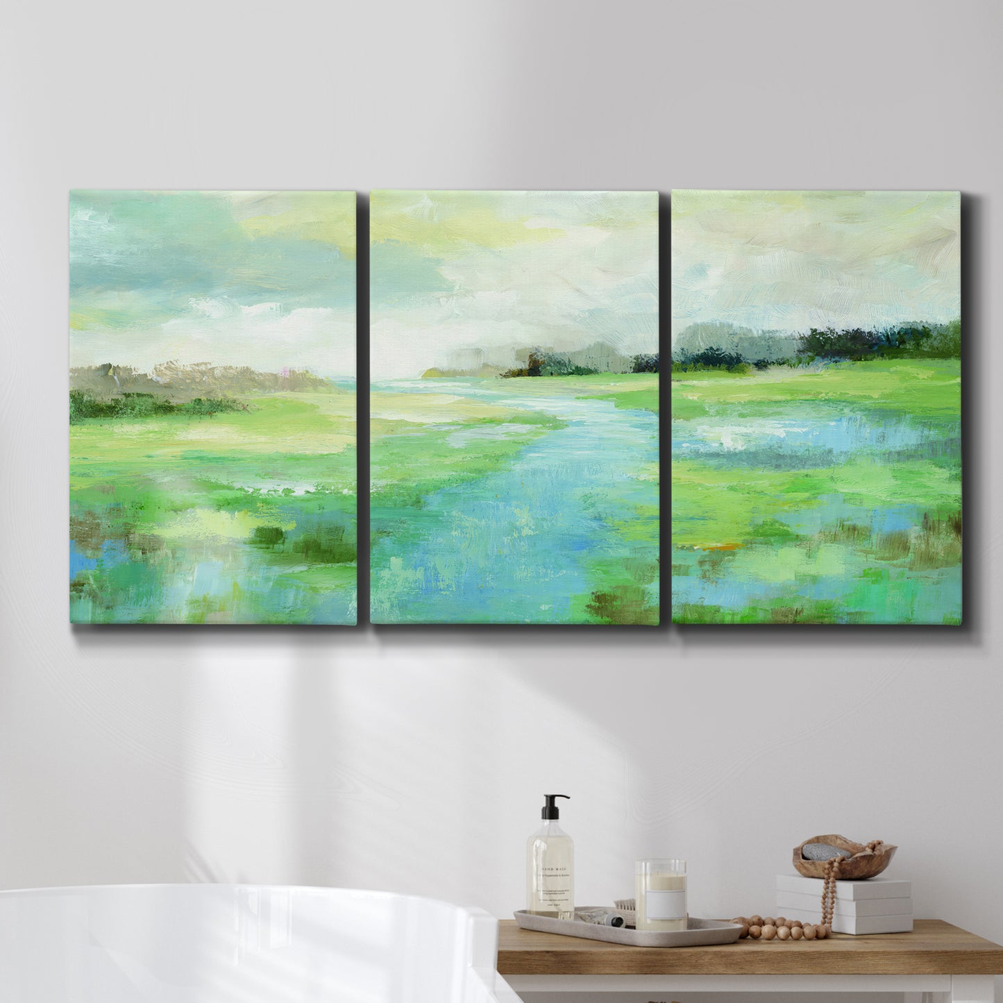 Three-panel canvas wall art featuring gentle stream winding through trees, displayed in a bathroom above a bathtub.