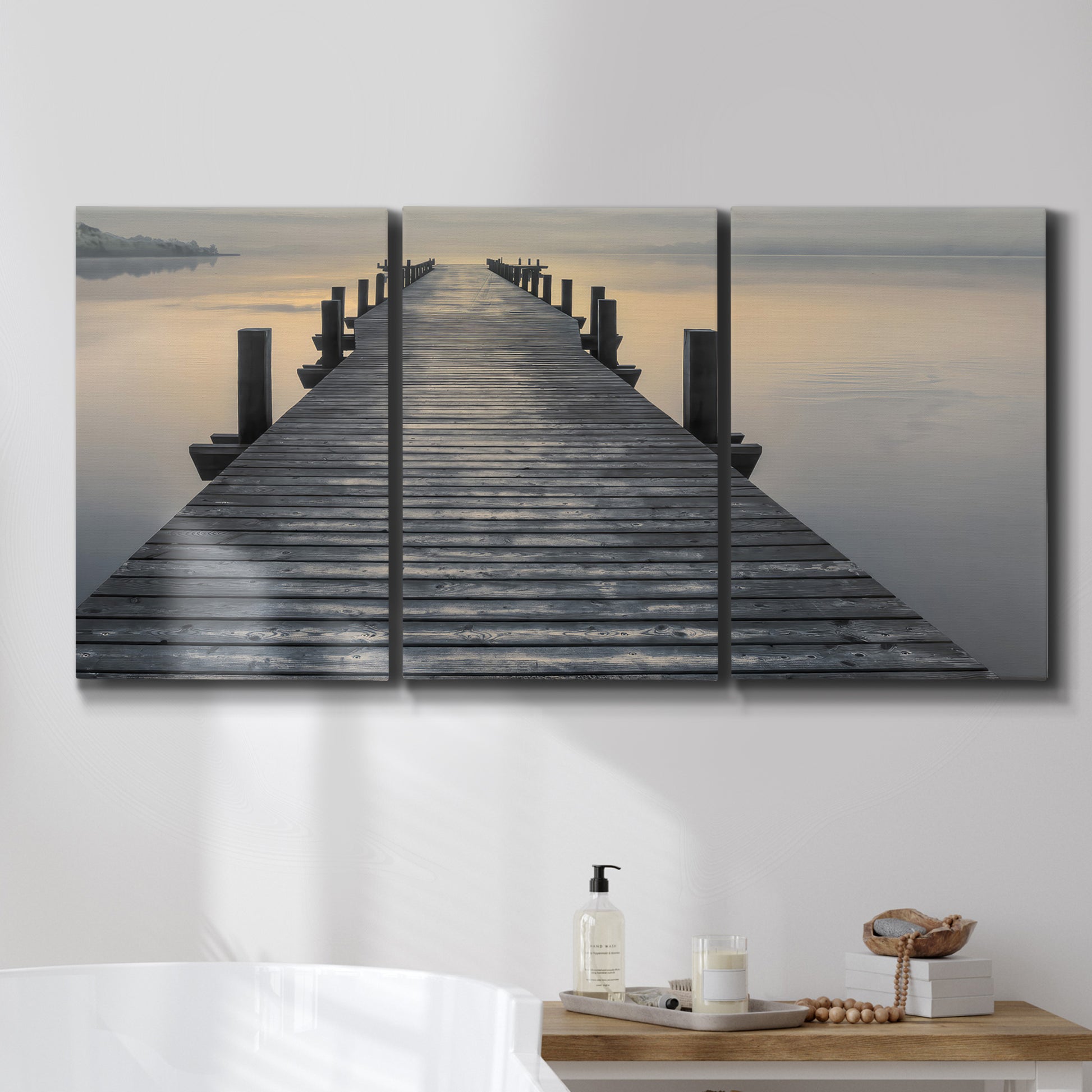 Three-panel canvas wall art featuring sunset over water photograph, displayed in a bathroom above a bathtub.