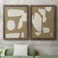 Set of two walnut barnwood framed canvas prints depicting a coordinated art pair of irregular white cutout-like shapes on taupe grounds rendered as bold minimalist shape abstracts above a sofa in a modern living room.