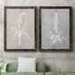 Set of two black barnwood framed canvas prints depicting a coordinated art pair of white botanical silhouettes on softly weathered neutral backgrounds rendered as rustic minimalist botanical prints above a sofa in a modern living room.