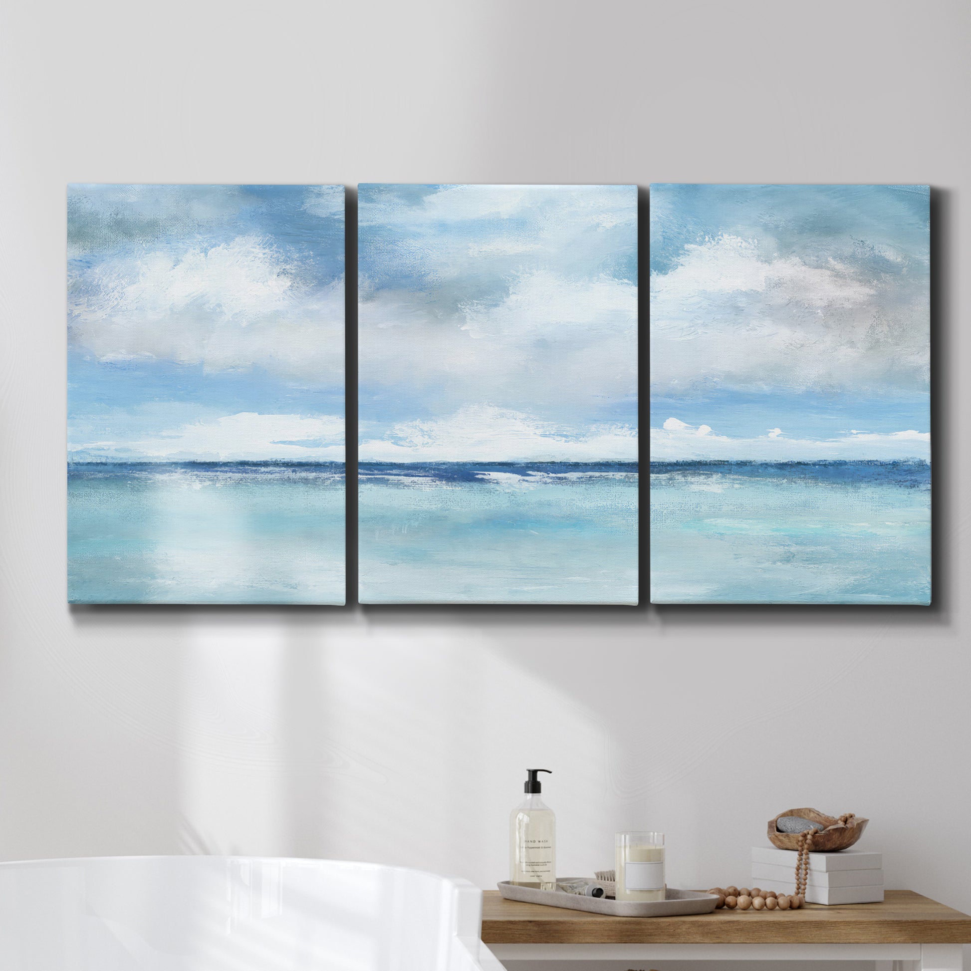Three-panel canvas wall art featuring tropical clouds over ocean horizon, displayed in a bathroom above a bathtub.