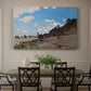 Canvas art print featuring a coastal beach scene with figures gathered along shoreline and boats nearby, showcased as a statement wall artwork