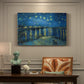 Canvas art print featuring a night scene with glowing stars reflected in river beside illuminated town, presented within a refined interior setting