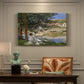 Canvas art print featuring a woman and child seated along riverbank beneath trees in soft daylight, presented within a refined interior setting